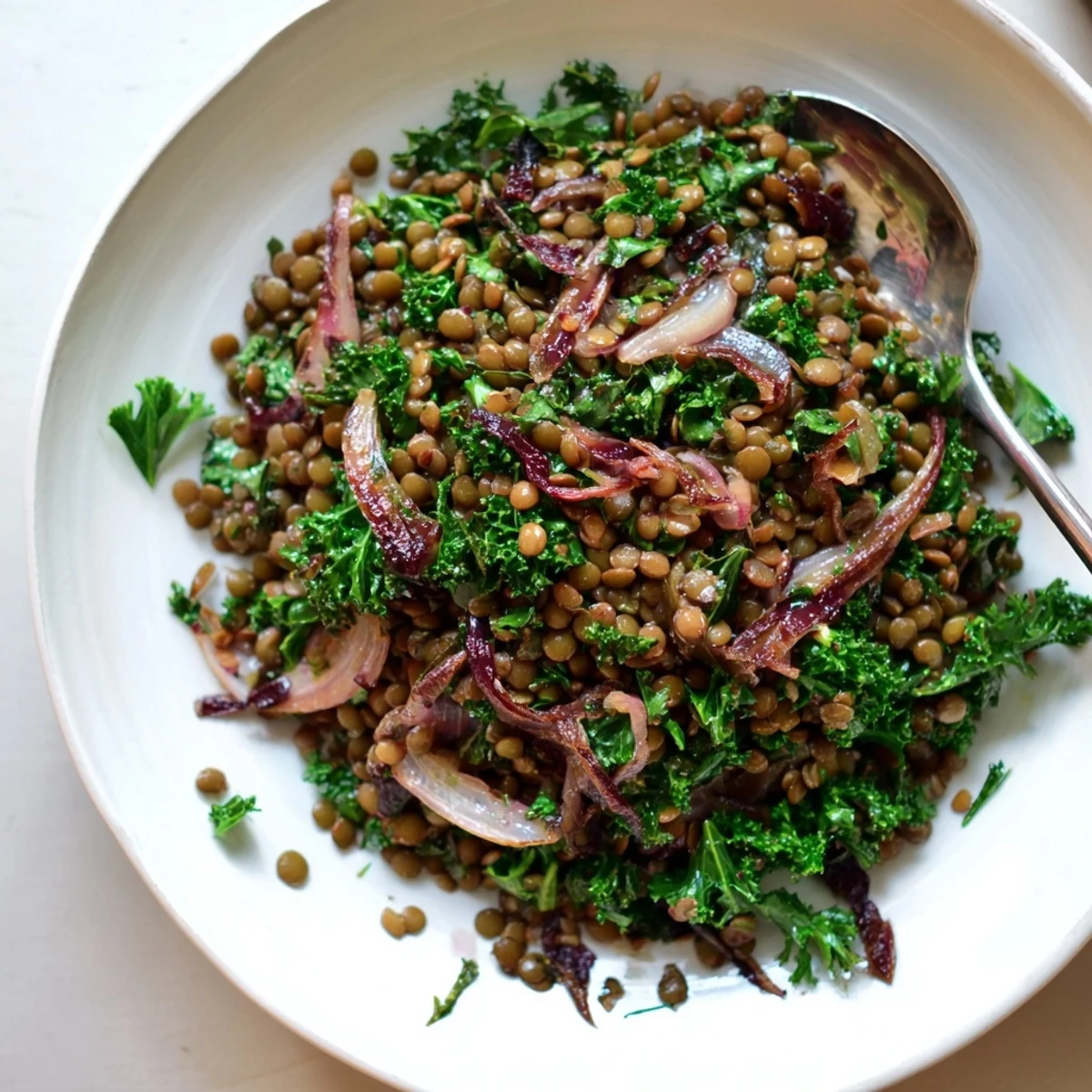 A close-up of warm green lentil salad, tossed with shallots and vinaigrette dressing.