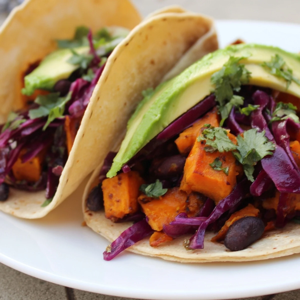 Tacos de patates douces et haricots noirs, garnis de crème végétale, feta et guacamole, parfaits pour un dîner en semaine.