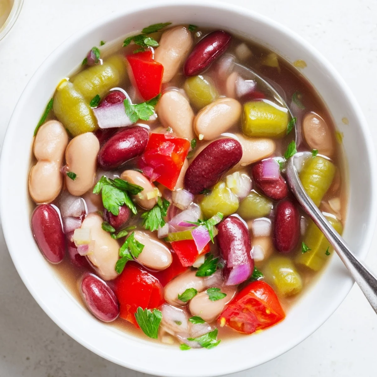 Une soupe Three-Bean Salad colorée dans une marmite, avec des haricots rouges et blancs, des haricots verts, du poivron rouge et des tomates cerises, parfait pour un repas réconfortant.