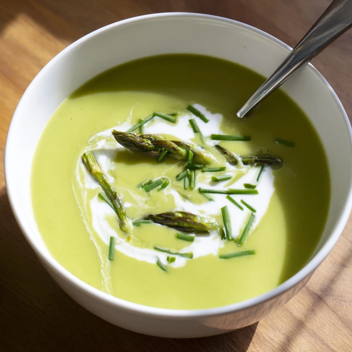 Silky Asparagus Soup ladled into a white bowl, garnished with blanched tips and lemon zest.