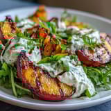 Salade d'été avec pêches grillées, burrata crémeux, roquette poivrée et glaçage balsamique.