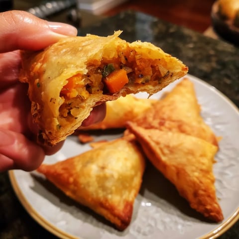 Une main tient une petite quiche ou un sandwich au dessus d'une plaque de marbre.