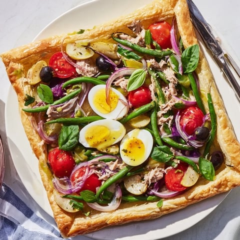 Tarte feuilletée Salade Niçoise colorée, avec légumes frais et thon savoureux.