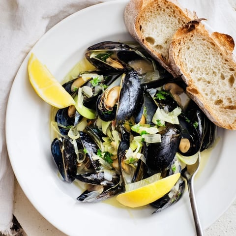 Moules Marinières dans un bouillon de vin blanc, servies avec du pain croustillant.