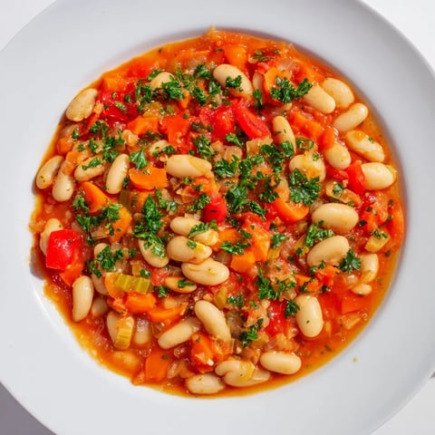 A steaming bowl of White Bean & Tomato Stew, garnished with fresh herbs, ideal for a comforting dinner.
