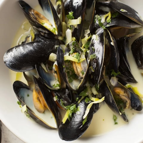 Classic creamy mussels swimming in white wine broth, ready to eat with crusty bread.