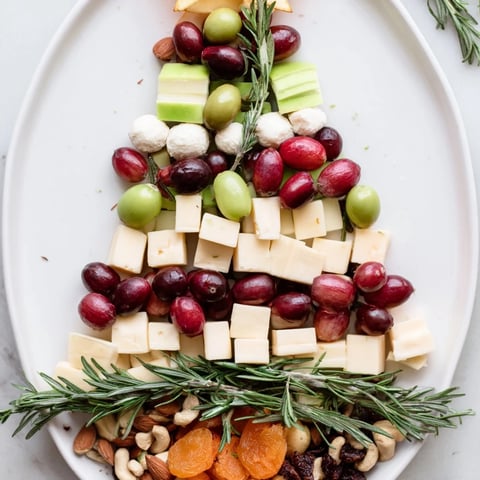 A Christmas-themed Cranberry Joy Tree Board features vibrant cheeses, fresh fruits, and crackers.