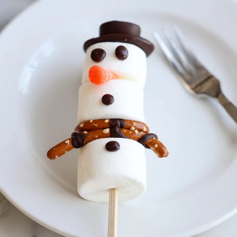 A close-up of Marshmallow Snowman Stick Arrangement, decorated with chocolate faces, pretzels, and orange noses.