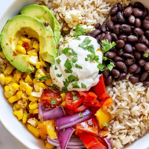 Steaming brown rice burrito bowl topped with vibrant veggies and creamy queso for a colorful meal.