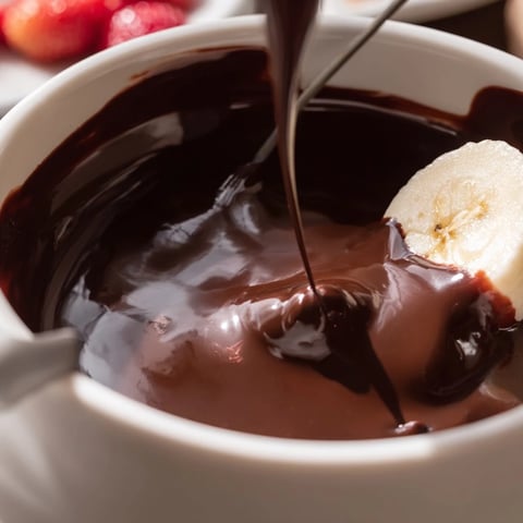 Un pot de fondue au chocolat fondu et crémeux, entouré de fruits frais, marshmallows et brioche pour tremper.