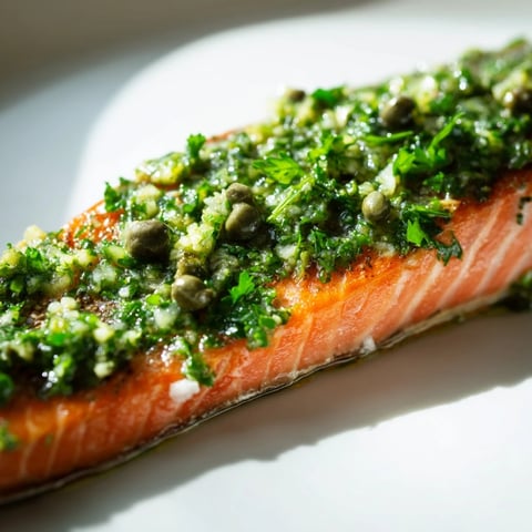 Roasted salmon fillets nestled with caramelized leeks and onions, finished with vibrant parsley dressing on a serving plate.