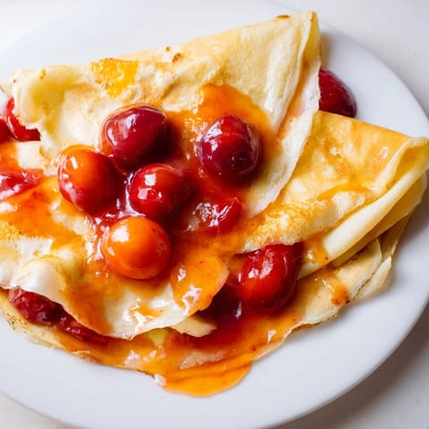 This image shows a beautifully plated Elegant Cherry-Coded Crêpe Suzette, perfect for a special occasion.