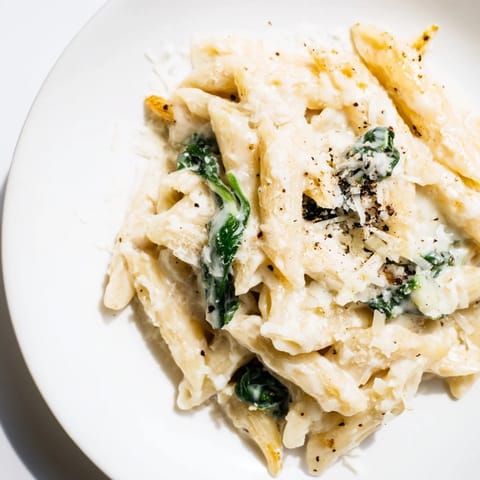 A close-up of creamy spinach pasta with wilted spinach, garnished and plated beautifully.