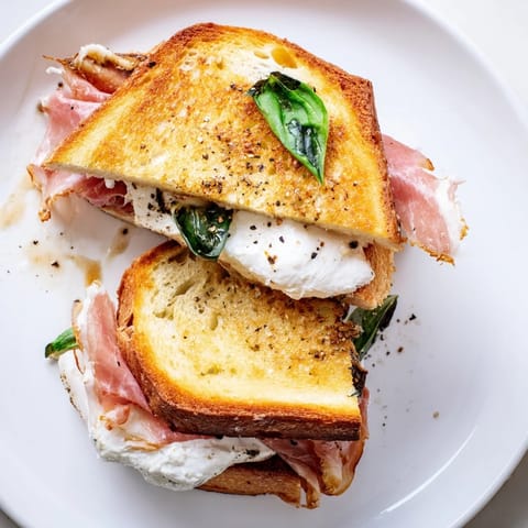 Melted burrata oozes out of a toasted Crispy Prosciutto & Burrata Grilled Cheese, ready to eat.