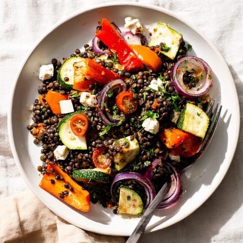 Une salade de lentilles noires avec légumes rôtis, servie tiède avec feta effritée et vinaigrette au citron pour un déjeuner méditerranéen.