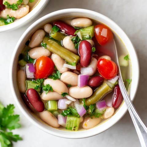 Une assiette de Three-Bean Salad Soup servie avec du pain grillé, parsemée de persil frais, inspirée de la salade classique aux trois haricots, une option végétarienne savoureuse.