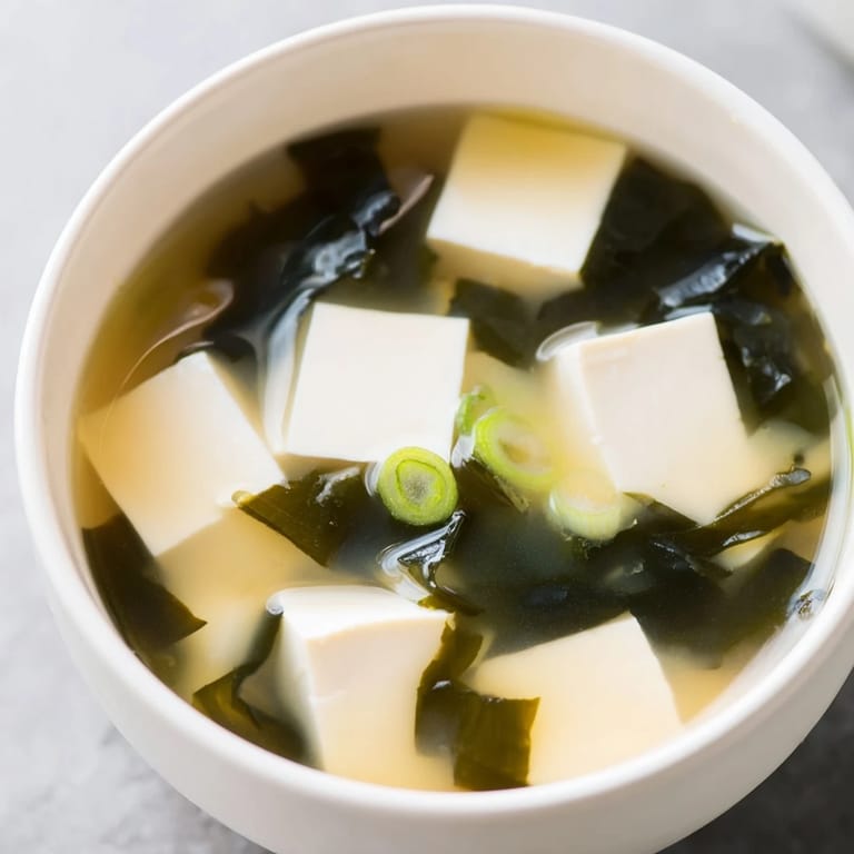 Soupe miso aux cubes de tofu, garnie de ciboulettes et d’algues, servie dans une bol en céramique.