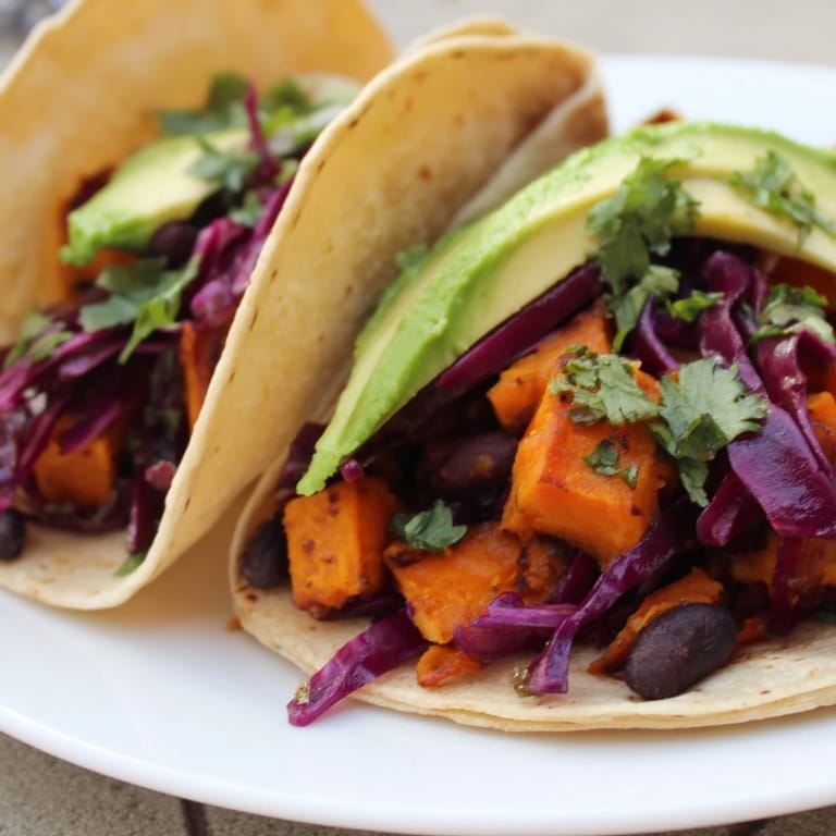 Tacos de patates douces et haricots noirs, garnis de crème végétale, feta et guacamole, parfaits pour un dîner en semaine.